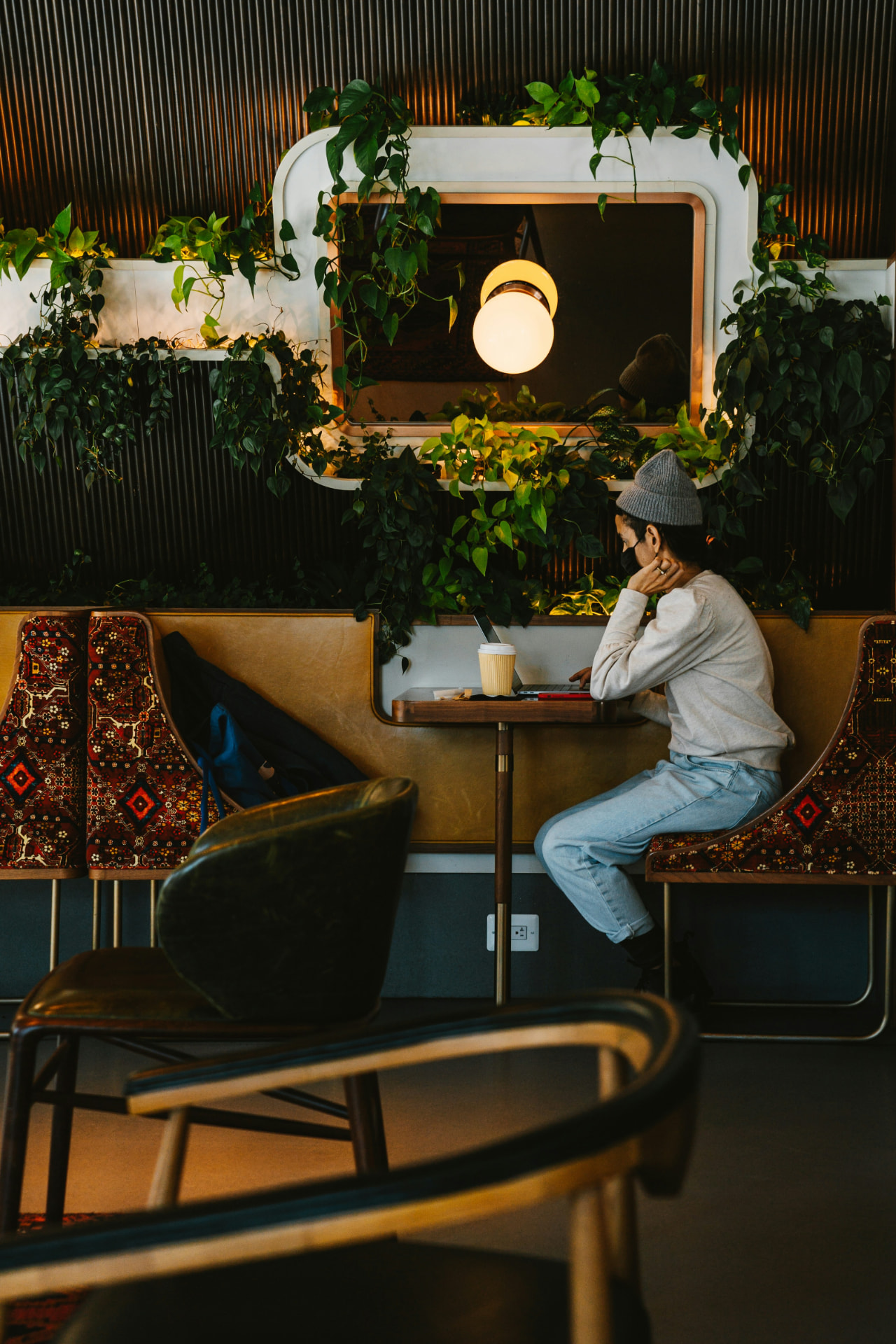 A person working on a laptop at a calm, plant-filled café table